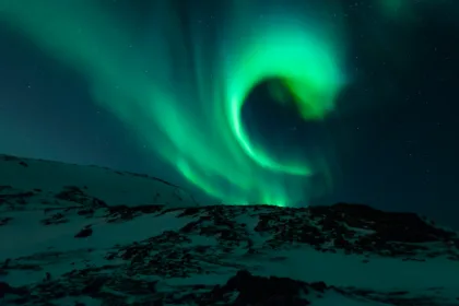 Aurora verde sobre un paisaje de montañas nevadas