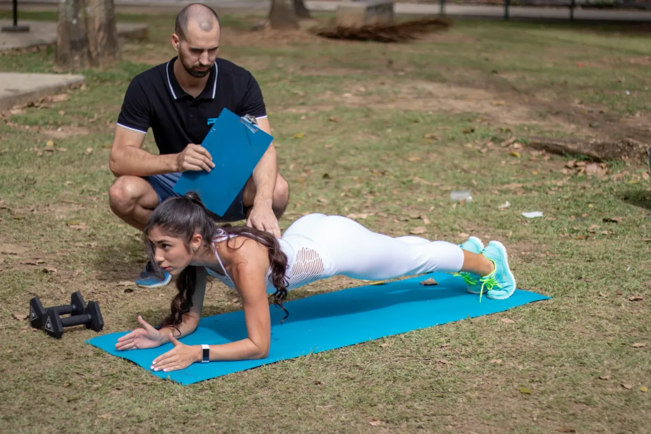 Una mujer realiza una plancha junto a un entrenador en un espacio exterior