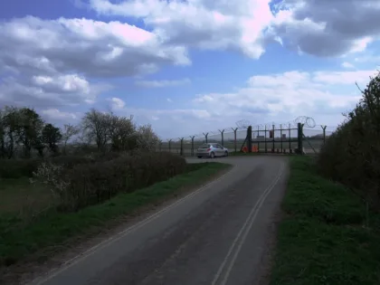 File photo of the entrance to RAF Fairford air base, with a road, a security fence, and the base grounds in the background. 2 April 2012.
