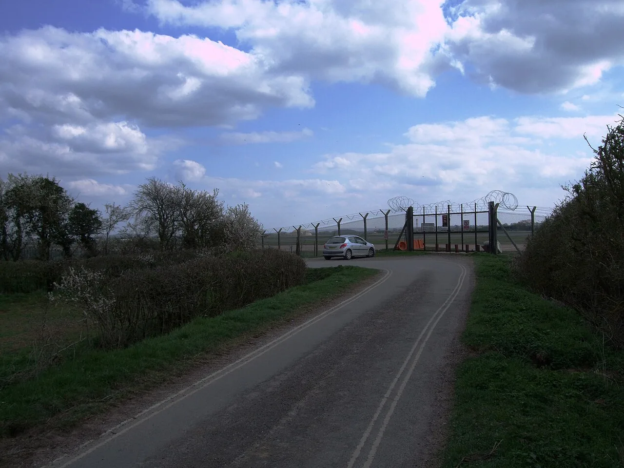 Foto de archivo del acceso a la base aérea RAF Fairford, con una carretera, una valla de seguridad y el terreno de la base al fondo. 2 de abril de 2012.