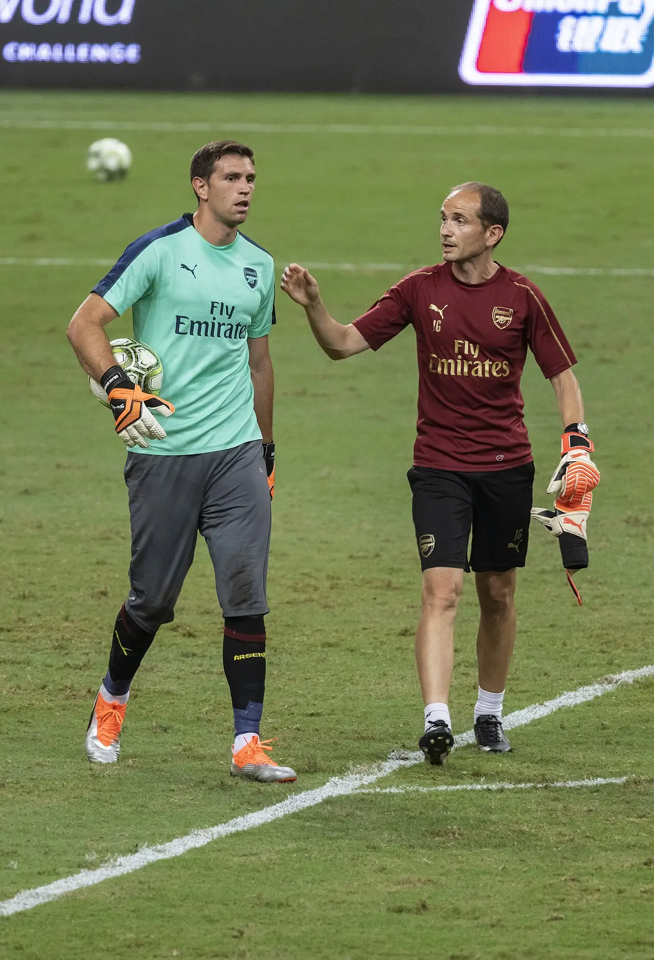 File photo from 28 July 2018: Emiliano Martínez, wearing Arsenal goalkeeper gear and holding a ball, appears on the field alongside another team member.