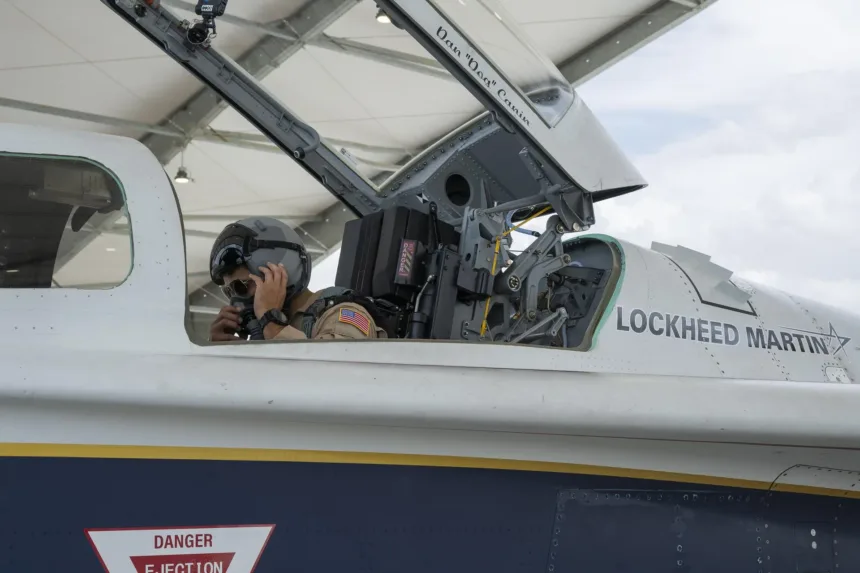 A test pilot adjusts his helmet in the open cockpit of the NASA X-59 experimental aircraft